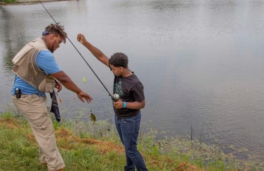 A young man helps a boy with a fish on his rod and reel